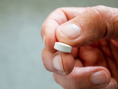 Close-up of a human hand holding a large white statin pill.