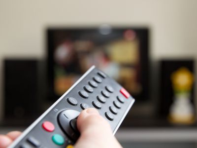 Human hand holding remote control changing Channels with television set.