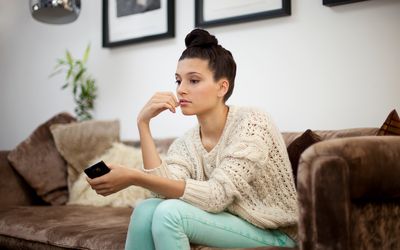 woman thinking on couch holding her phone