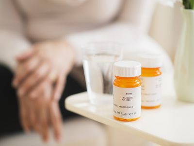 two pill bottles and glass of water with woman in background