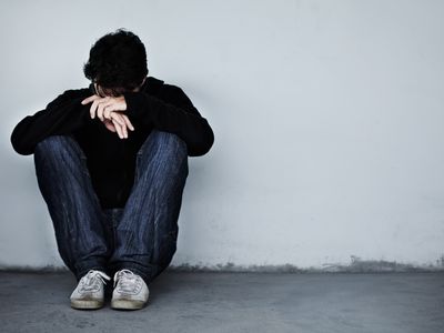 upset young man sitting against wall with head on hands