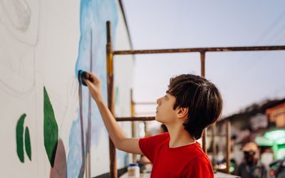 child doing an artistic wall painting in a city