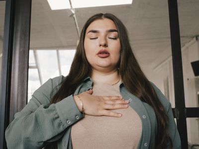 Young businesswoman with eyes closed and hand on chest at office