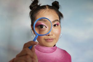 Teenage girl with magnifying glass against colored background