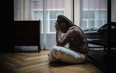 Young woman sits on the floor near bed and looks very upset and stressed