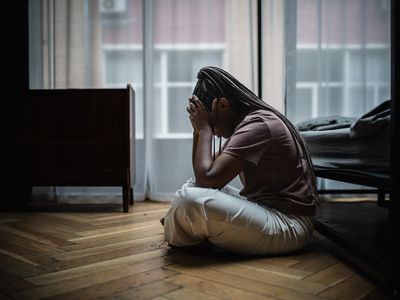 Young woman sits on the floor near bed and looks very upset and stressed