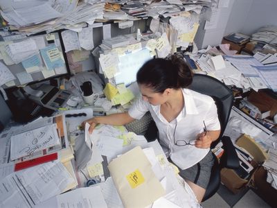 Businesswoman looking through papers on cluttered desk, elevated view