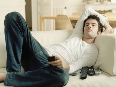 Man relaxing on sofa holding remote controls