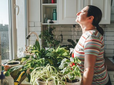 woman deep breathing exercises in own home garden among plants