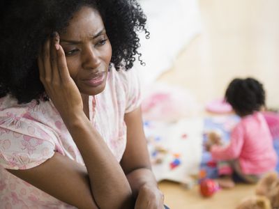 Frustrated mother rubbing her temples while child plays in background