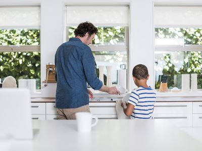 Rear view of father and son cleaning dishes in kitchen at home