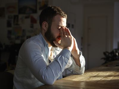 Young man sitting at kitchen table with hands on face