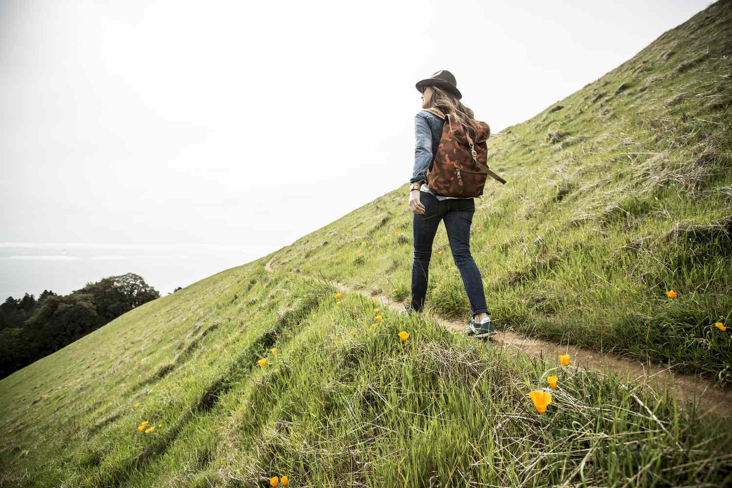 A woman with a backpack and hat on standing at a lookout