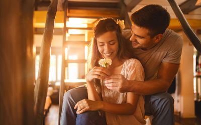 Affectionate man surprising his girlfriend with a carnation flower while sitting on staircase at home.