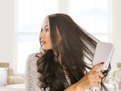 Woman brushing long dark, wavy hair with a large, flat hairbrush