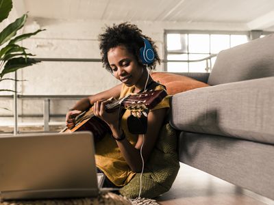 Young woman at home with headphones and laptop playing guitar