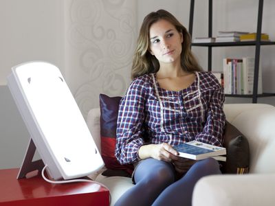 A woman sitting next to a light therapy box