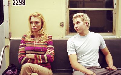 Young couple sitting apart in subway car, man looking at woman 