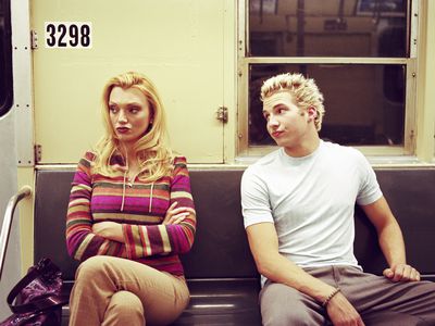 Young couple sitting apart in subway car, man looking at woman 