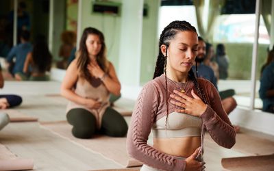 Young woman meditating with her eyes closed and touching her chakras during a yoga class