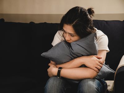 Depressed asian woman sitting on sofa holding a cushion