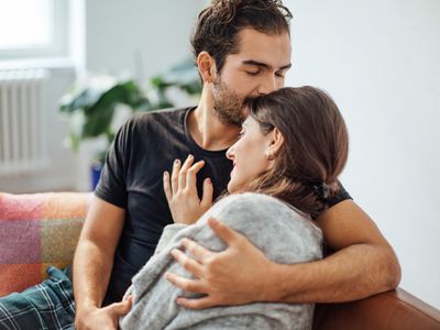 Young man embracing girlfriend while kissing on her forehead in living room at home