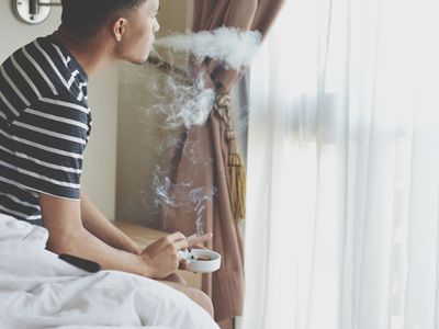 Man Smoking Cigarette While Relaxing On Bed