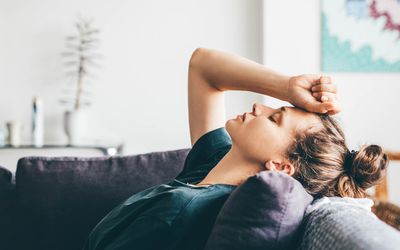 woman lying on the couch with her fist on her forehead looking tired.