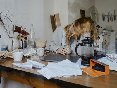 woman sitting at messy desk, slightly blurry with her head in her hands