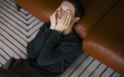 person lying halfway on the ground and halfway on the couch with hands covering eyes