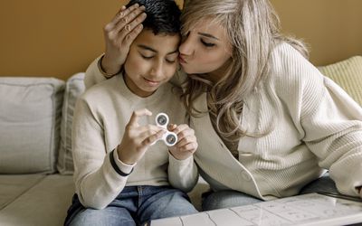 mother kissing son on the forehead, little boy is holding a fidget spinner