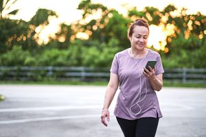 Mature woman walking at sunset carrying a mobile phone