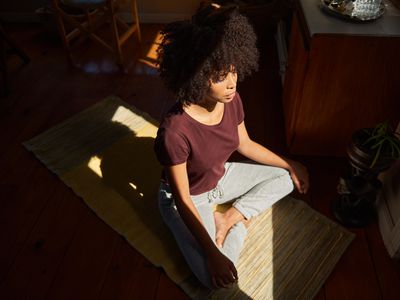 High angle view of a young African woman meditating in a ray of light on the floor of her living room