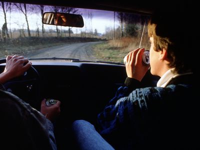 person in car driving holding a beer