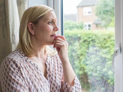 Sad Woman Suffering From Agoraphobia Looking Out Of Window