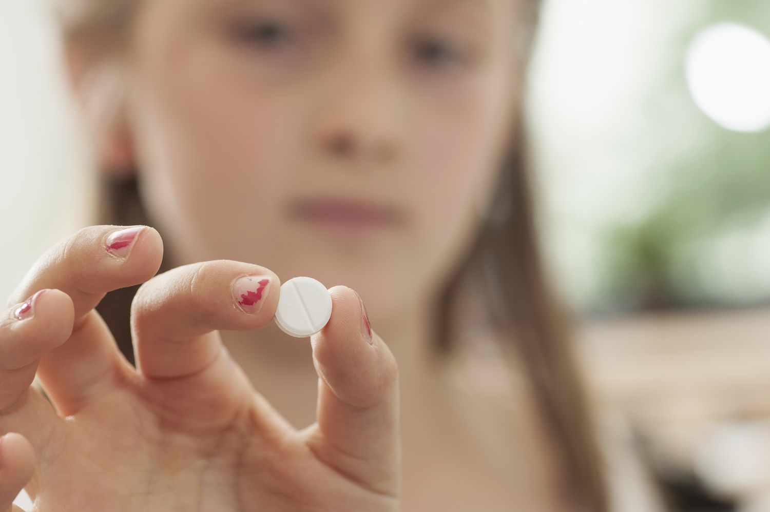 Young girl holding an ADHD pill between her thumb and forefinger