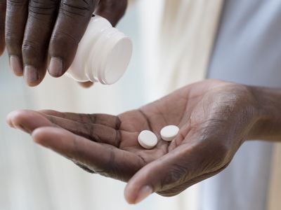 Black person pouring pills out of a bottle into their hand