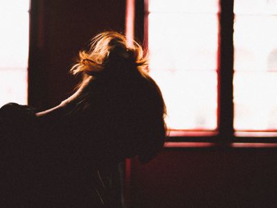 Silhouette of woman with her head down in front of window