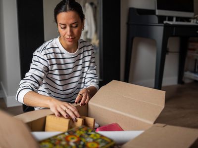 Young woman sitting on the floor at home organizing a moving box