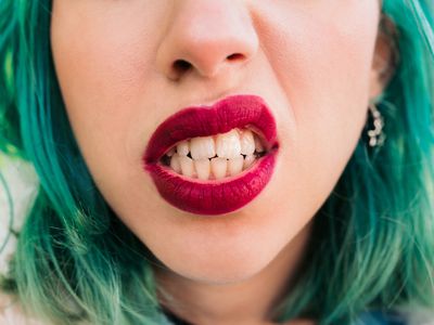 Detail of the mouth of a young woman with green hair and red lips making an aggressive gesture and showing her teeth. 