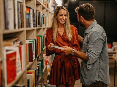 Side view of a smiling man and woman in the book store, looking for a good book to read.