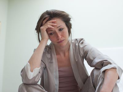 Depressed woman in pajamas sitting in bed