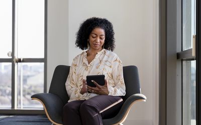 Therapist looks down at tablet while sitting in chair in room with large windows