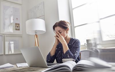 Tired, stressed businesswoman at laptop with head in hands