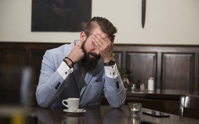 Tired man in suit covering eyes with hand