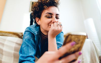 Young woman, with short, curly hair, using phone, in her apartment, lying upside down.