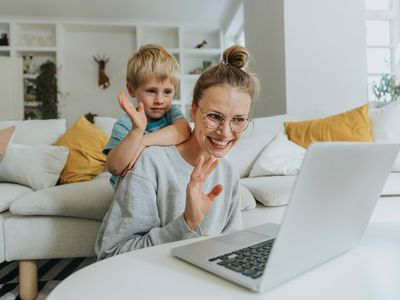 Mother and son waving hand to video call on laptop while sitting at home