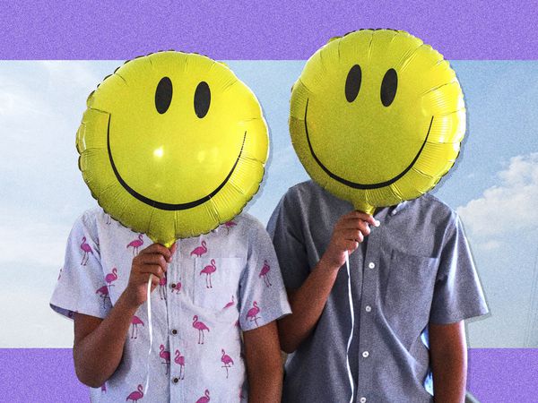 two people holding smiley face balloons over their face