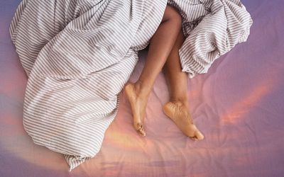 Slim, perfect and beautiful crossed woman legs on bed at vacation and holiday. Cropped of erotically lying on bed african american lady in bedroom and crumpled white bed clothes, top view, empty space