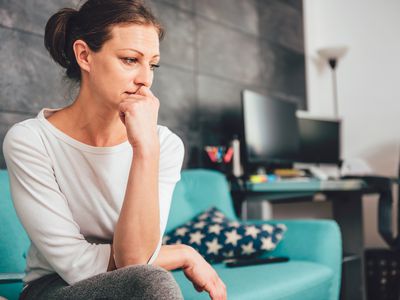 Worried, anxious, middle-aged woman sitting on her couch at home